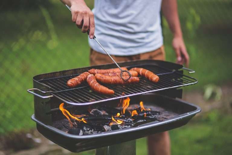 Mann brät Würstchen auf einem Grill an