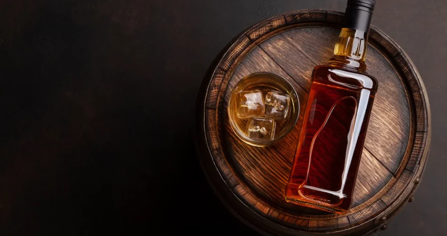 Whiskey Flasche und Glas mit Whiskey und Eiswürfeln liegen auf einem Fass