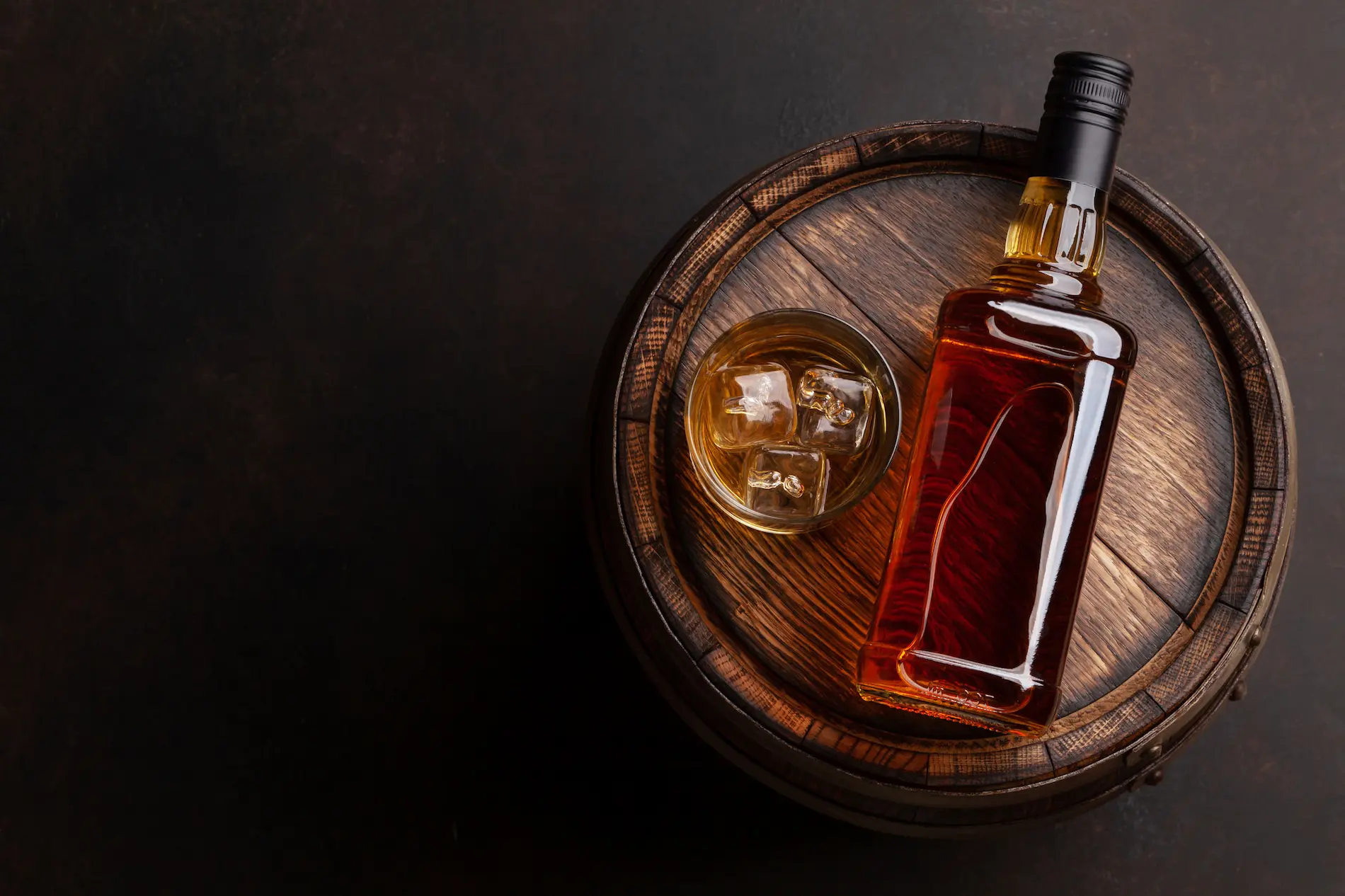 Whiskey Flasche und Glas mit Whiskey und Eiswürfeln liegen auf einem Fass